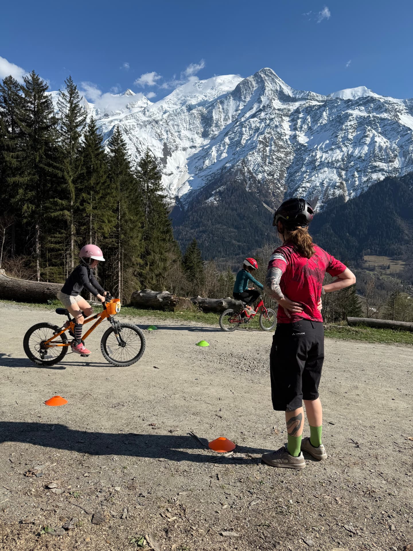 Coach GLOW encadrant deux jeunes vététistes sur un parcours de cônes face aux montagnes
